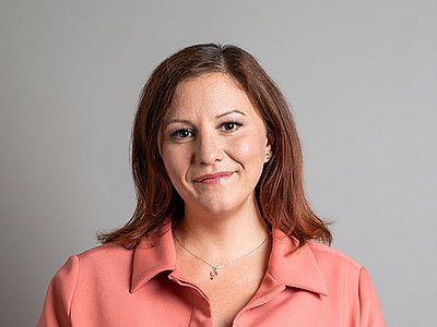 Claudia Papesch steht vor einem hellgrauen Hintergrund, trägt eine apricot-farbige Bluse und blickt freundlich ein die Kamera.
